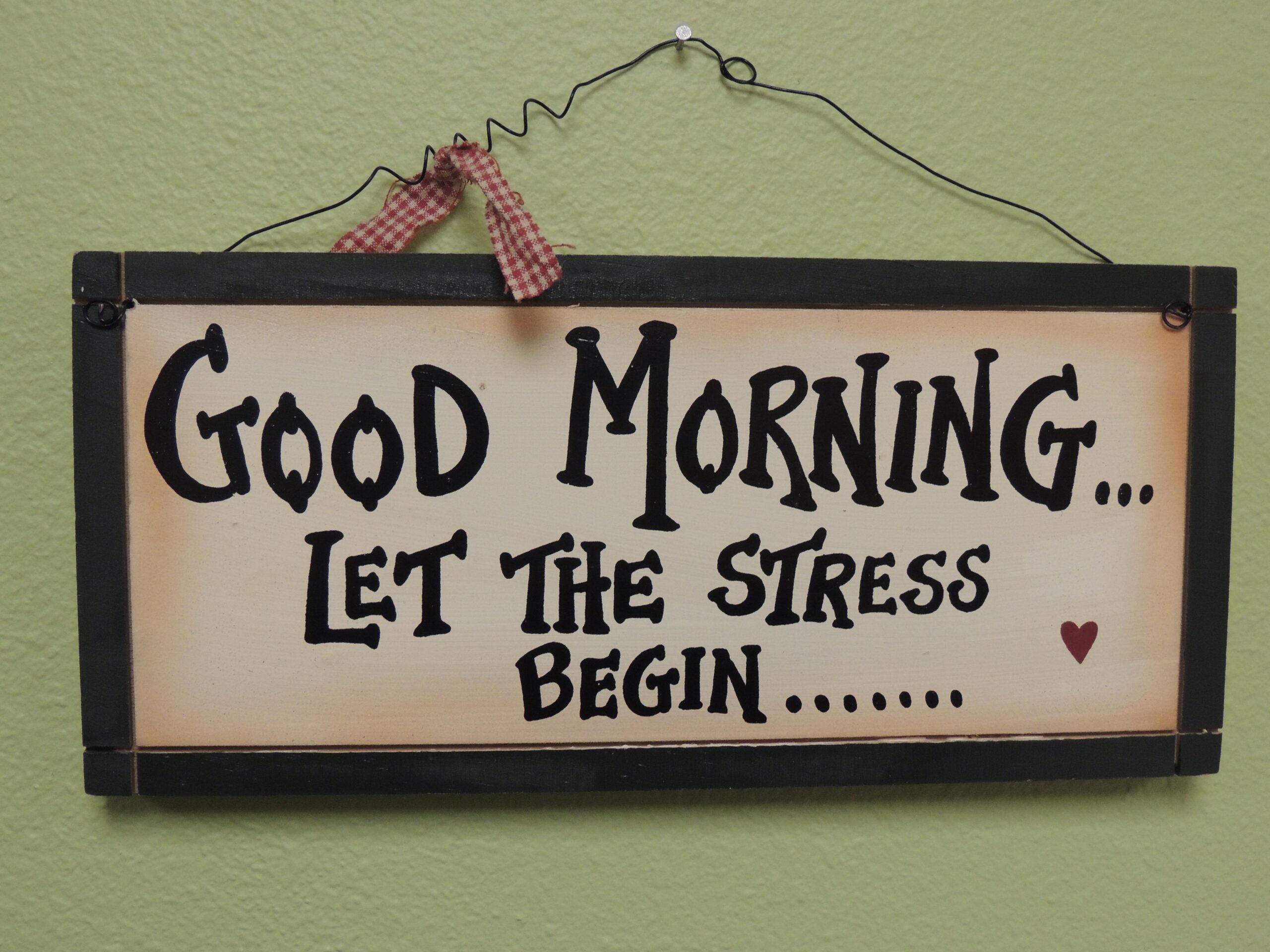 A sign hanging on a bright green wall says "Good Morning...Let the Stress Begin...."