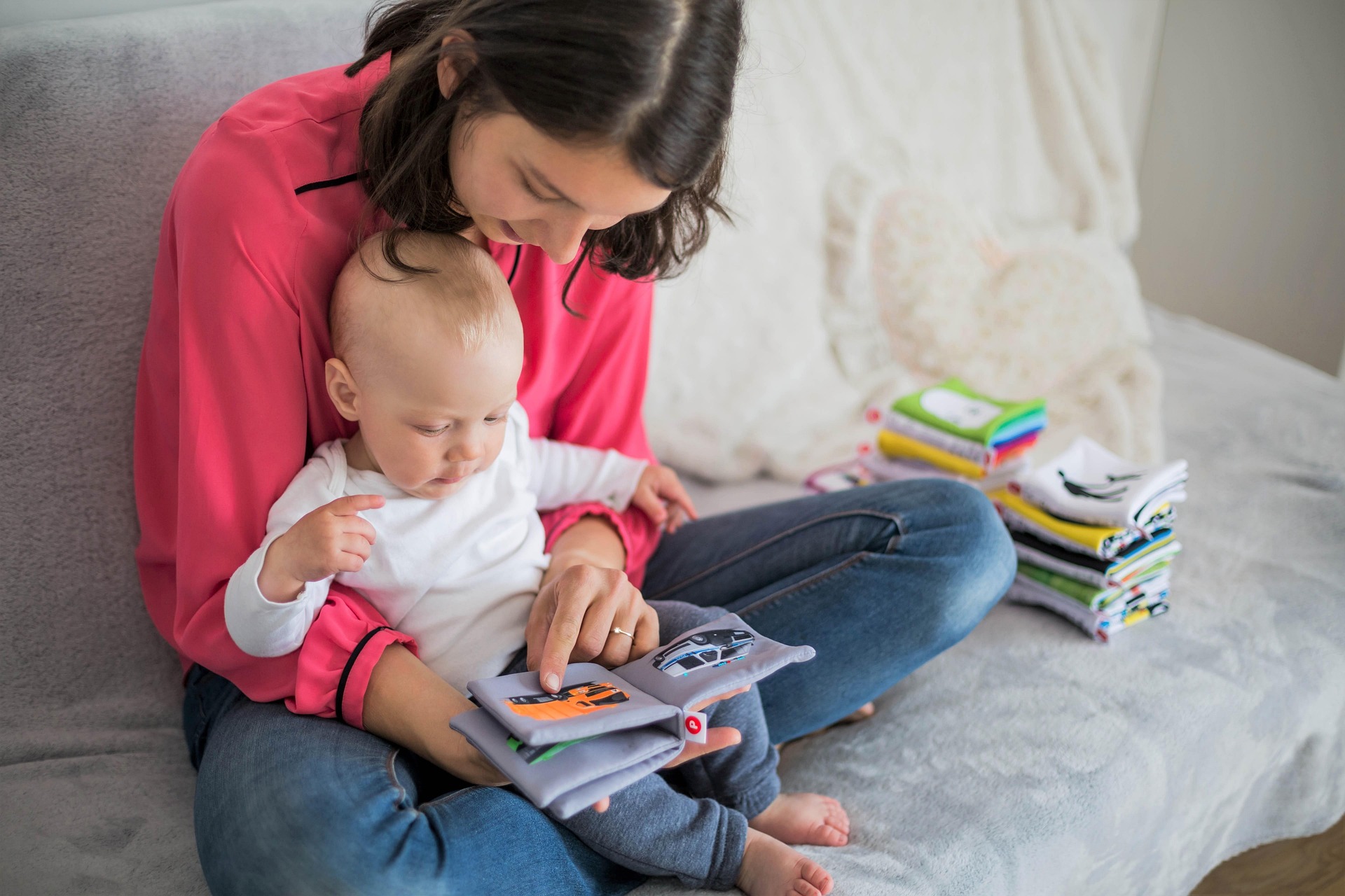 A parent sits holding a child while she reads board books
