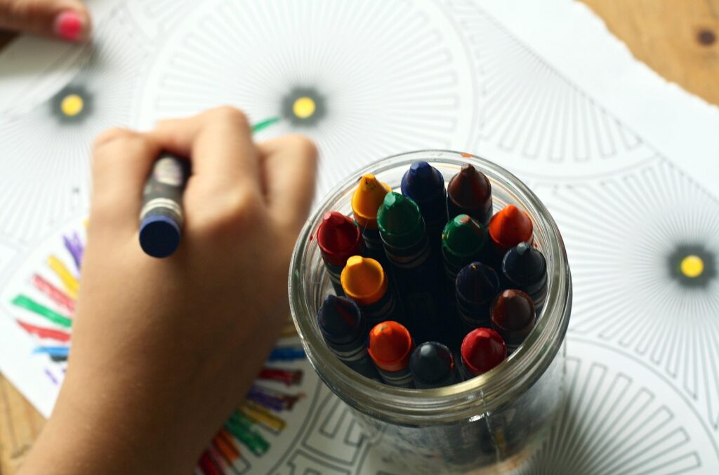 A jar with crayons and a small hand coloring with a gray color. 